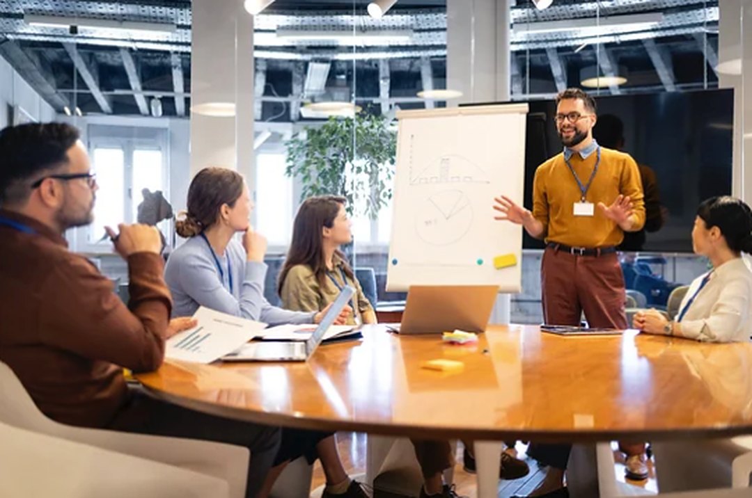 A coach presenting at a flip chart to a group seated around a conference table